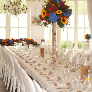 Kompozycje kwiatowe na stołach gości na brzozowych stojakach